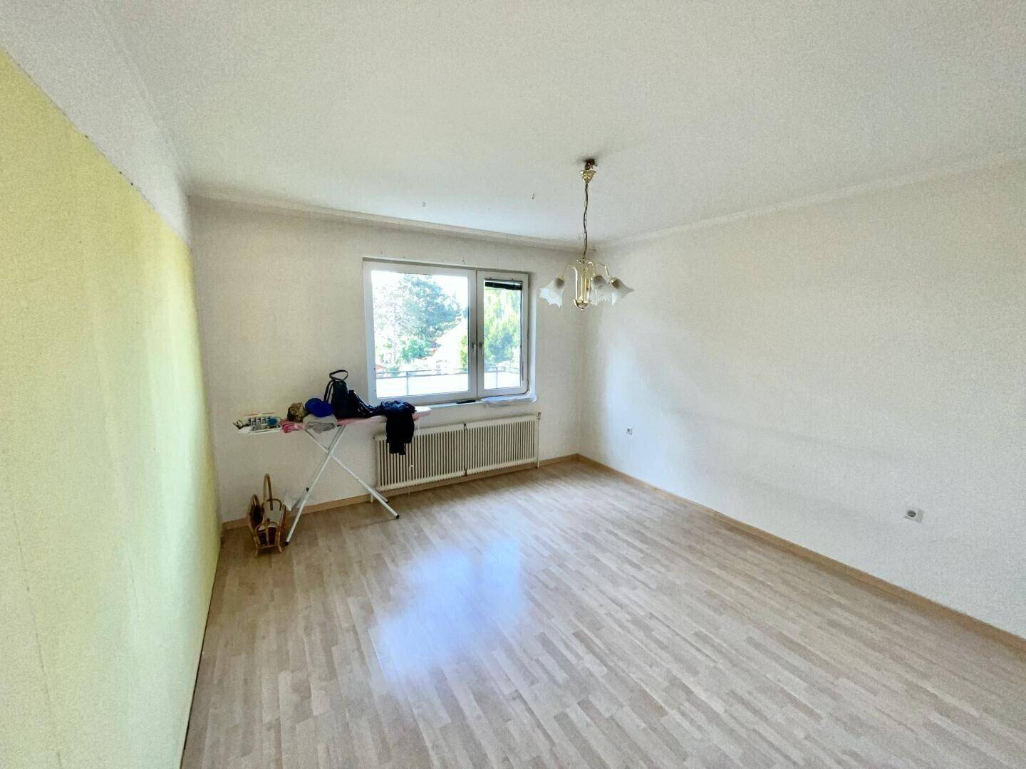 Helles Zimmer mit hellem Holzfußboden und großem Fenster, ideal als Schlaf- oder Arbeitszimmer.