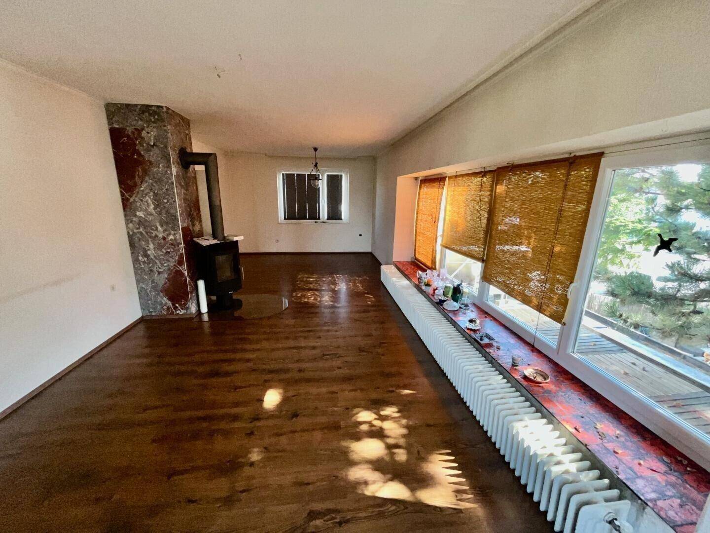 Geräumiges Wohnzimmer mit Kaminofen, Holzboden und breiter Fensterfront für viel Tageslicht.