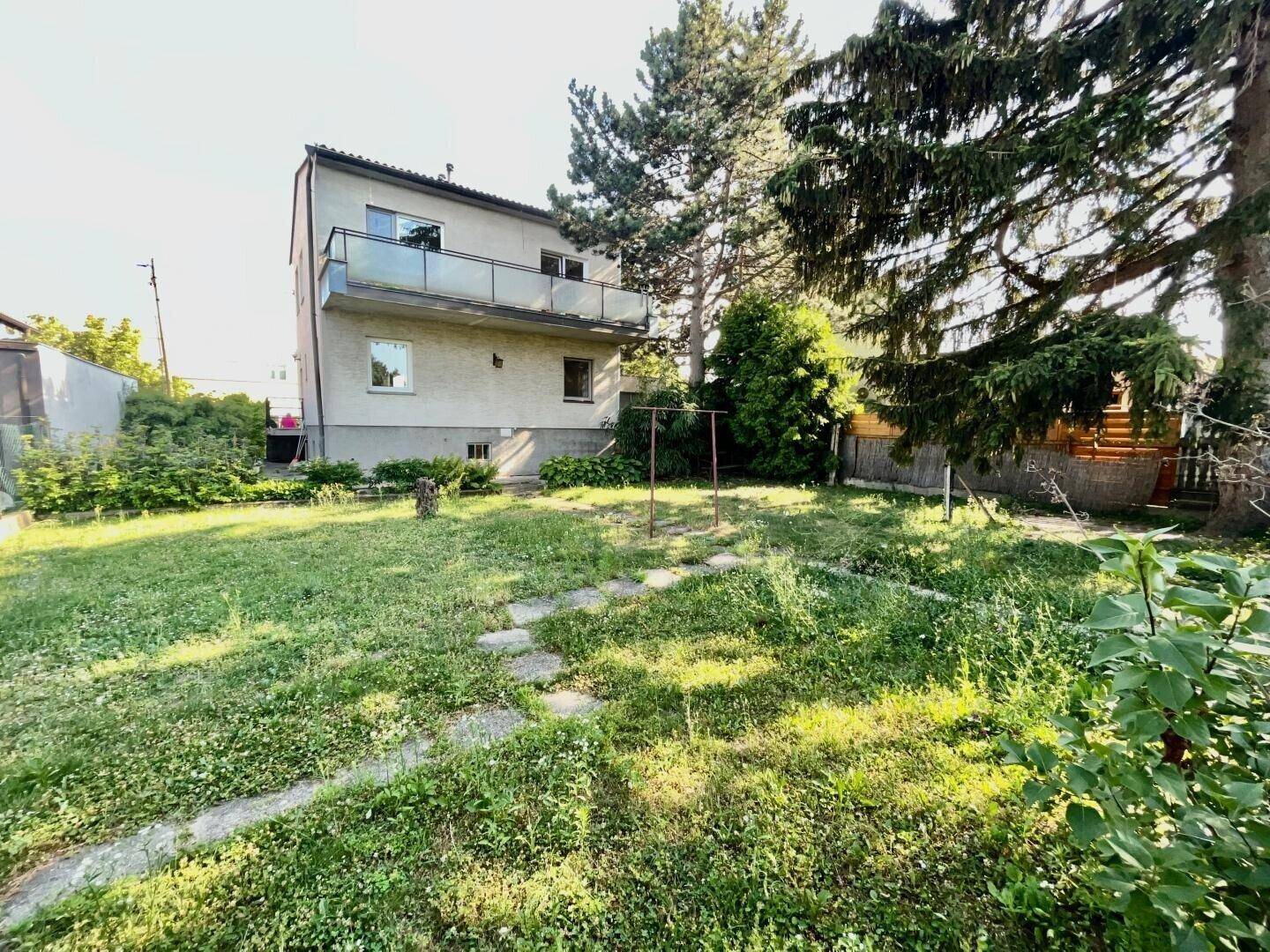 Rückansicht des Hauses mit großem Garten und Wäscheleine, umgeben von Bäumen.