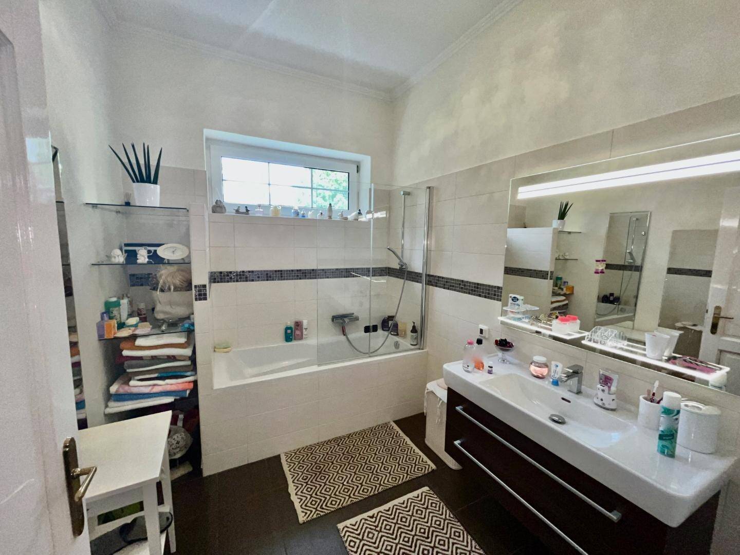 Helles Badezimmer mit Badewanne, großem Waschtisch und Fenster für Tageslicht.