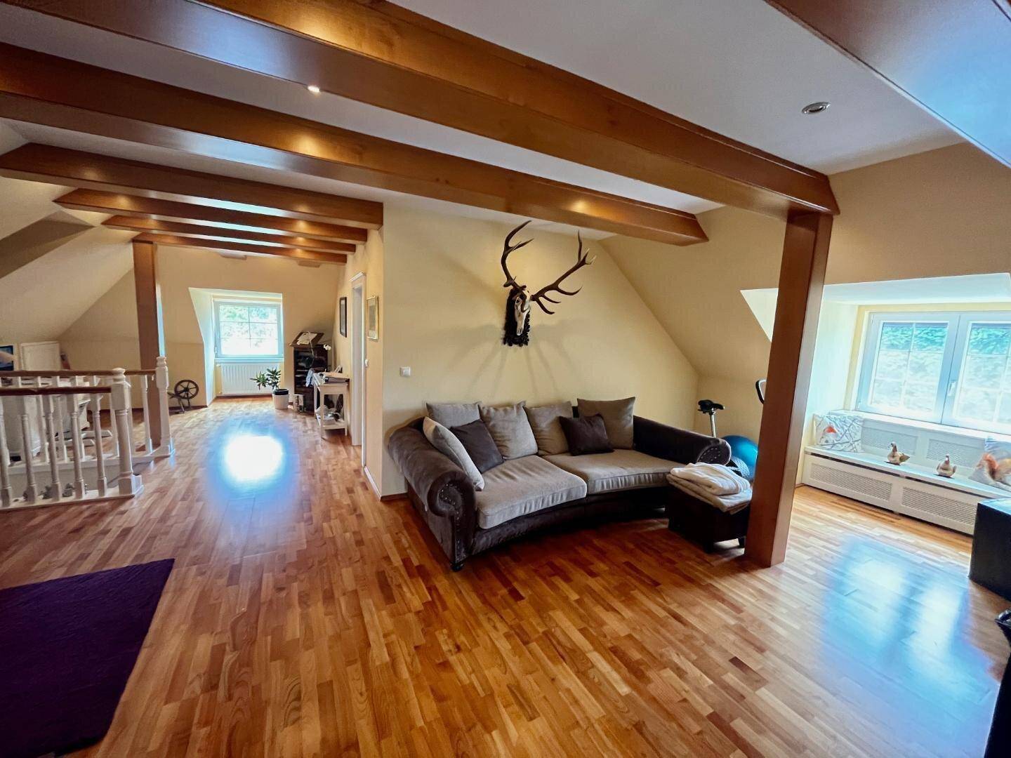 Geräumiger Dachboden mit Holzbalken, bequemer Couch und traditioneller Hirschgeweih-Dekoration.