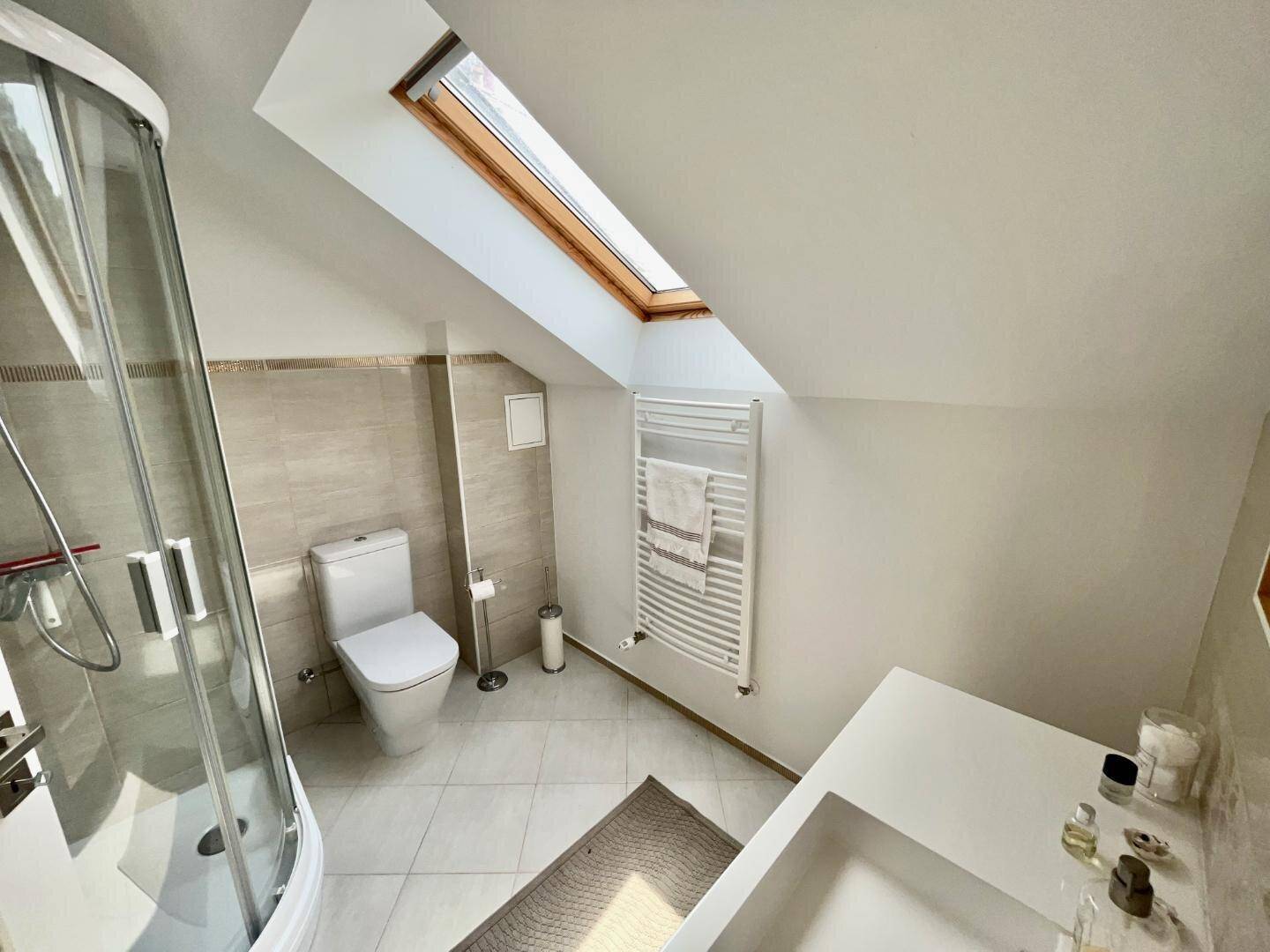 Modernes Badezimmer im Dachgeschoss mit Duschkabine, WC, Waschbecken und einem Dachfenster.