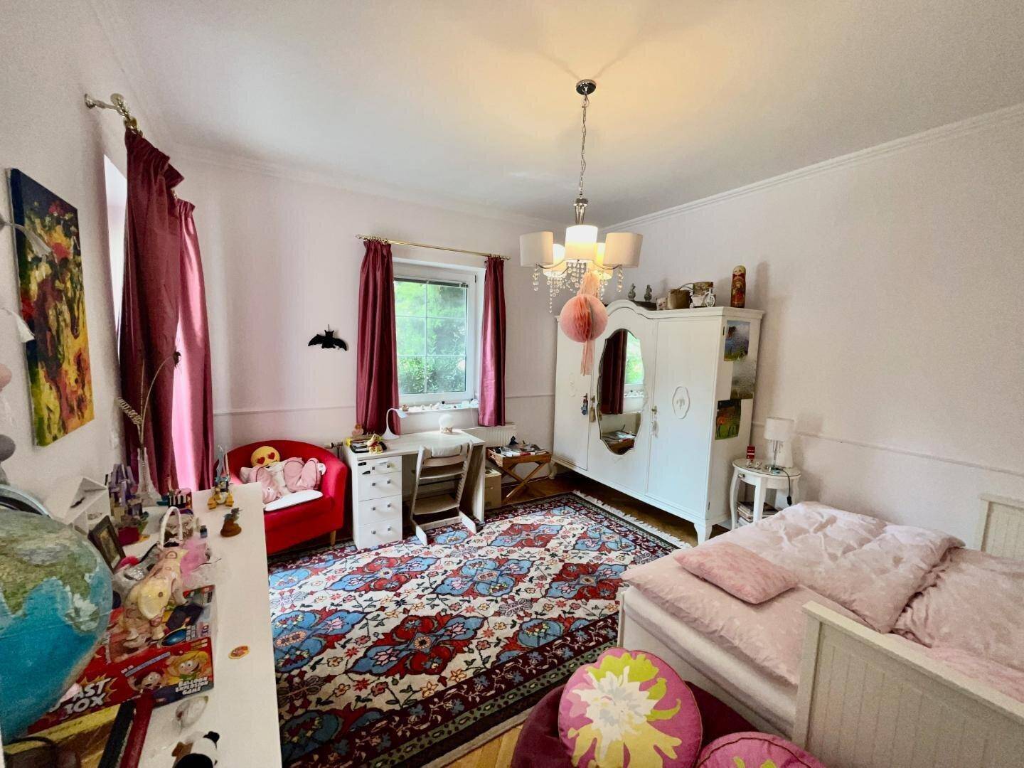Kinderzimmer mit farbenfrohem Teppich, Einzelbett und Schreibtisch am Fenster.