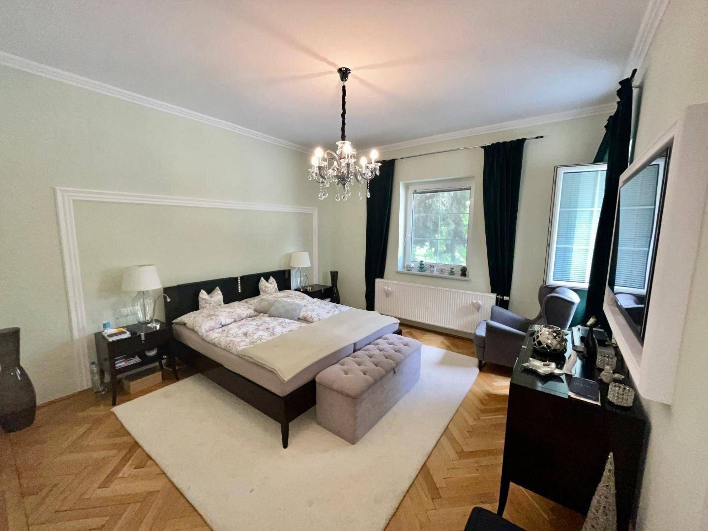 Helles Schlafzimmer mit Fischgrätparkett, einem Kronleuchter und einem großen Doppelbett.