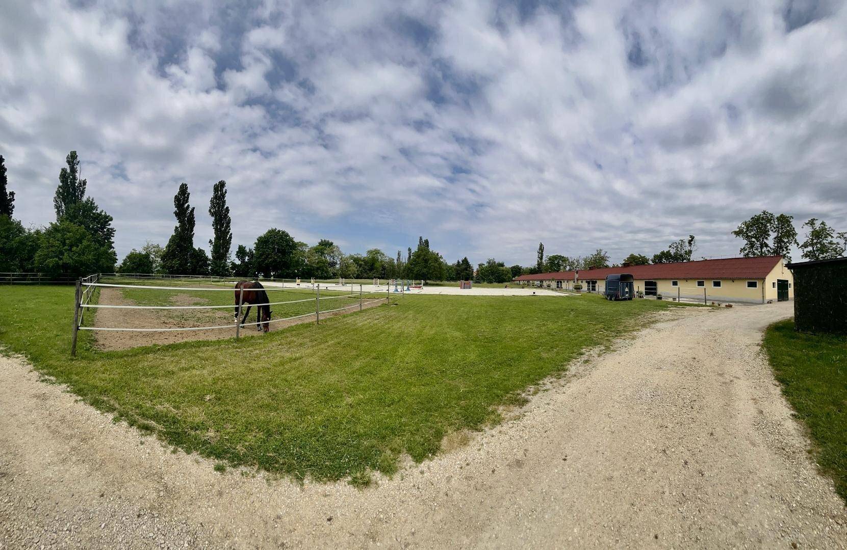 Panoramablick auf das weitläufige Anwesen mit Pferdekoppeln, Stallungen und viel Grün.