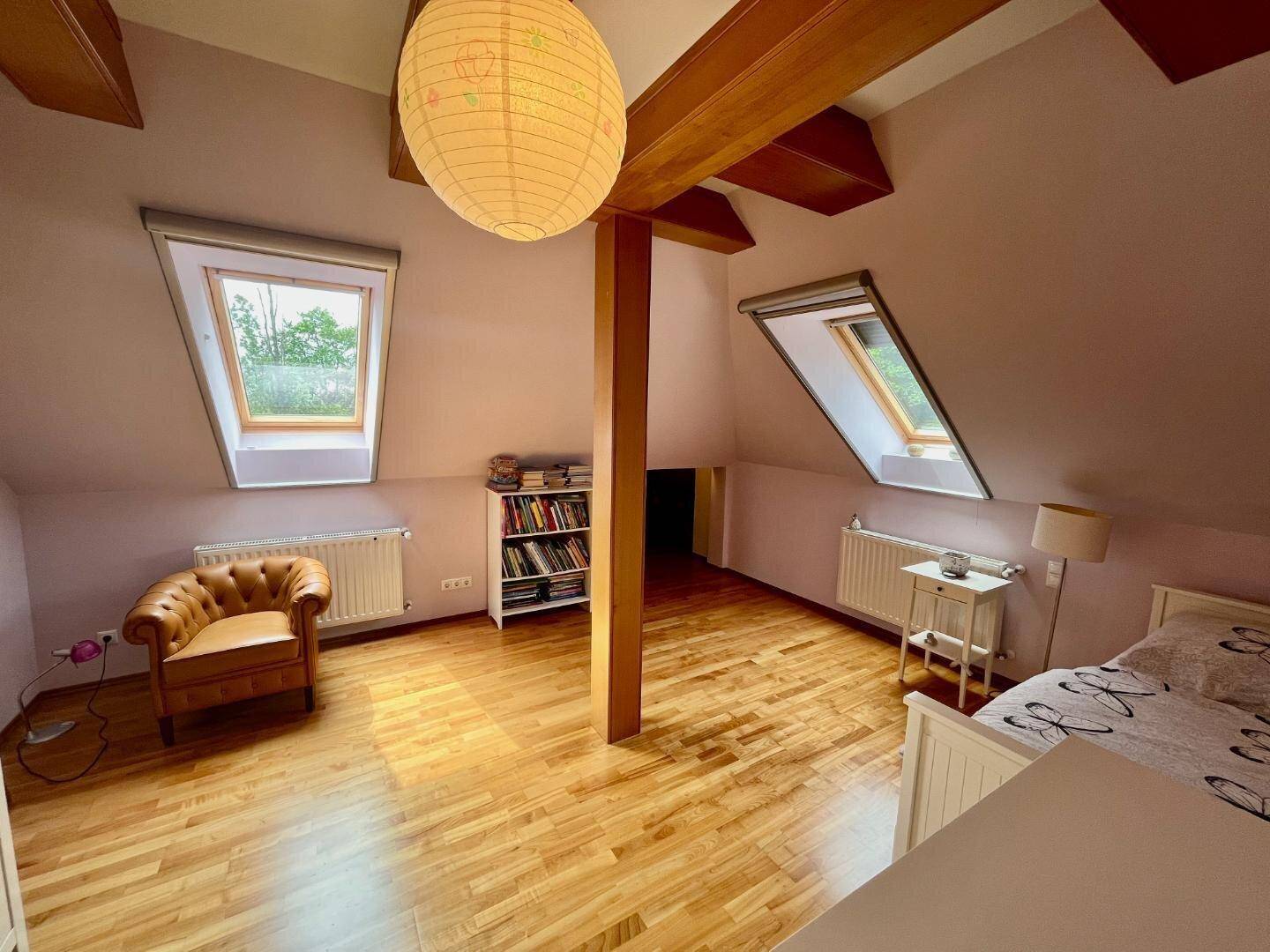 Helles Schlafzimmer im Dachgeschoss mit schrägen Wänden, Dachfenstern und Holzboden.