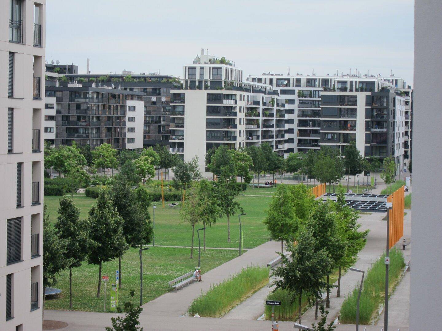 Weitläufige Grünanlage mit Bäumen und Wegen, umgeben von modernen Wohngebäuden.
