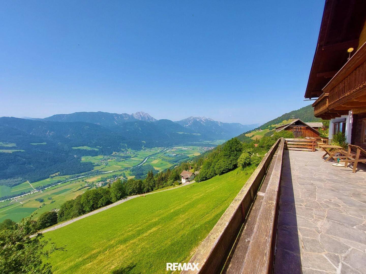Weitläufige Terrasse mit Panoramablick auf die grüne Berglandschaft und das sonnige Tal.
