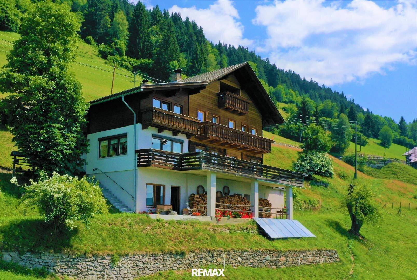 Traditionelles Chalet mit Holzfassade und Balkonen, eingebettet in eine grüne Hügellandschaft.