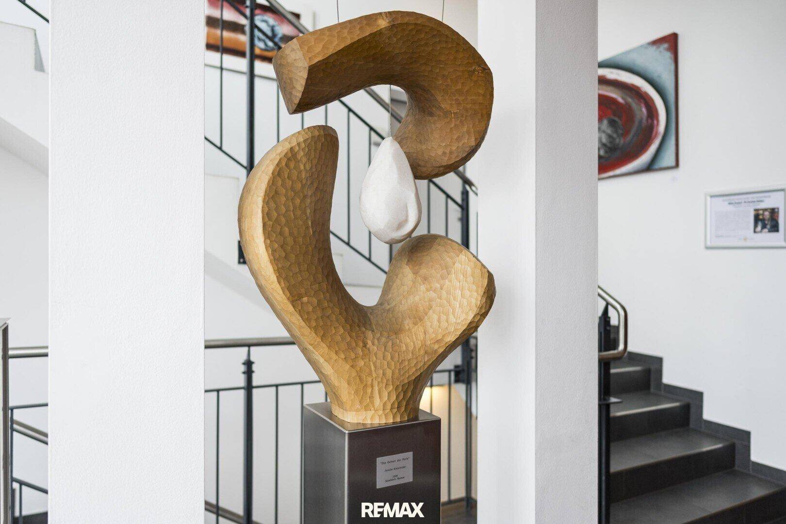 Abstrakte Holzskulptur in einem hellen Treppenhausbereich mit moderner Kunst an den Wänden.