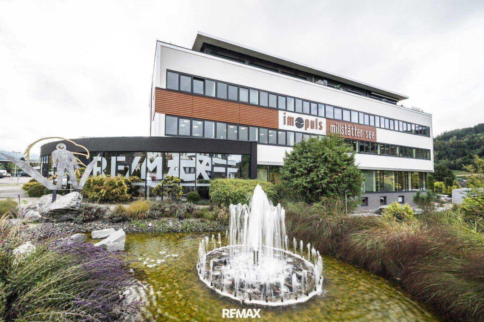 Modernes Geschäftsgebäude mit ansprechender Außenanlage, Springbrunnen und gepflegter Bepflanzung im Vordergrund.