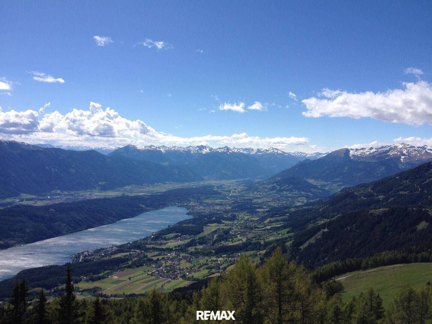Spektakulärer Panoramablick auf ein weites Tal mit See, Stadt und schneebedeckten Bergen.