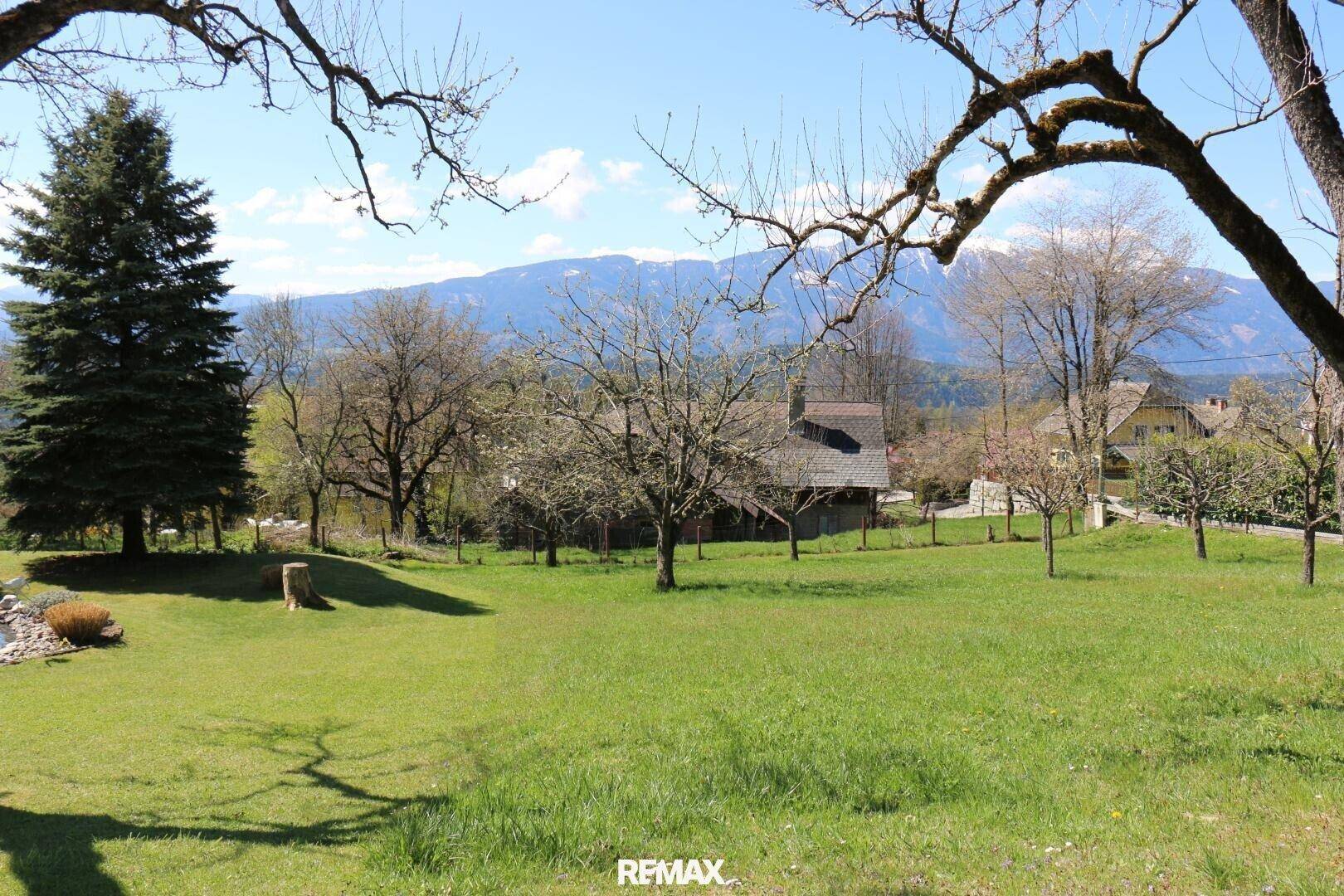 Weitläufiger grüner Garten mit Bäumen und einem malerischen Blick auf die umliegende Berglandschaft.
