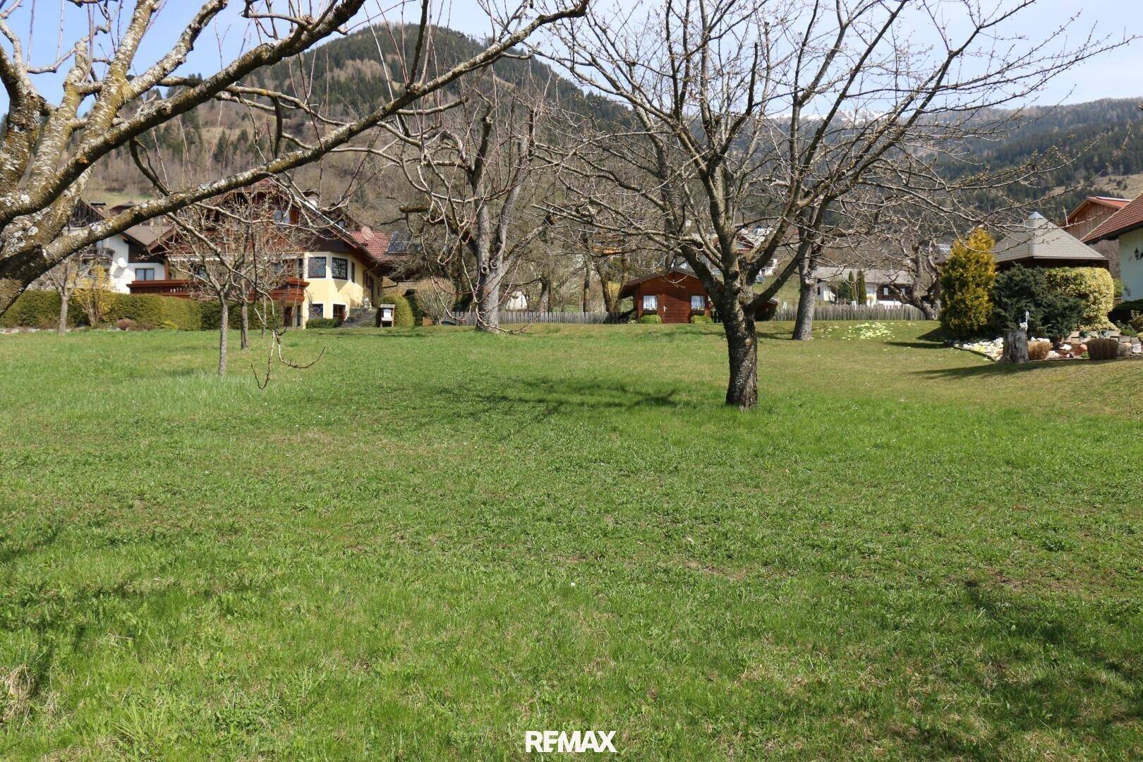 Weitläufiger grüner Gartenbereich mit Bäumen und Häusern, eingebettet in eine ruhige Hügellandschaft.