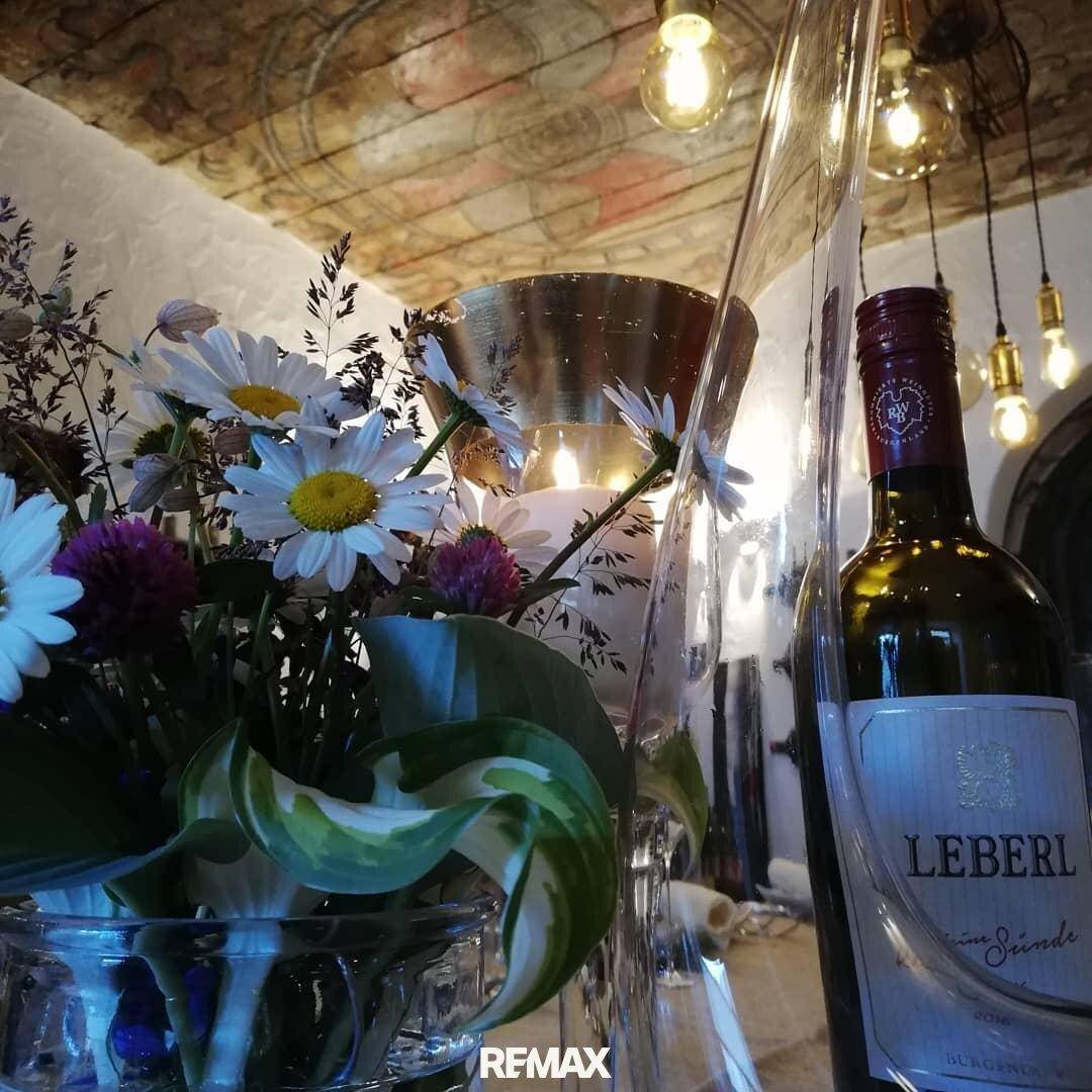 Detailaufnahme einer Tischdekoration mit frischen Blumen und einer Weinflasche unter einer kunstvoll bemalten Decke.