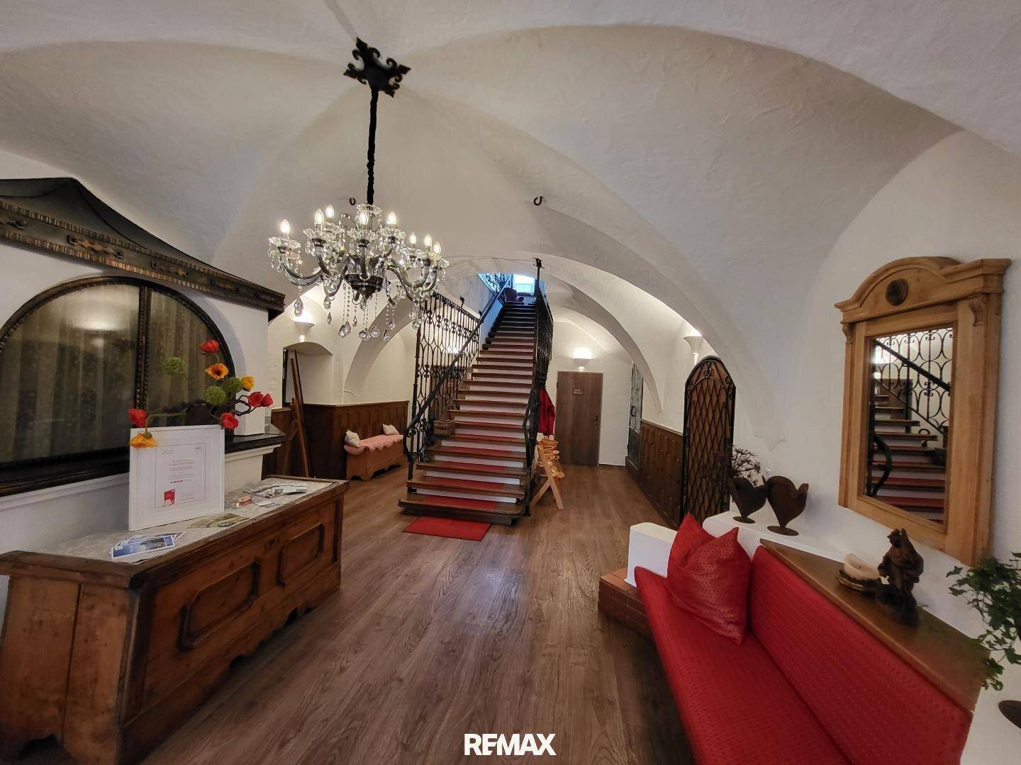 Eindrucksvoller Eingangsbereich mit geschwungener Treppe, Kronleuchter und historischen Gewölbedecken.