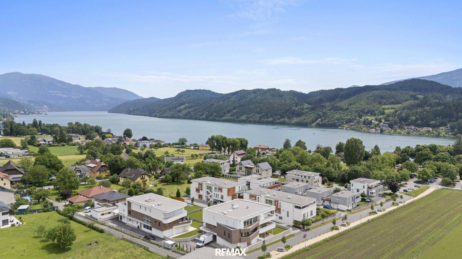 Luftaufnahme einer modernen Wohnsiedlung mit Blick auf einen See und die umliegende Berglandschaft.