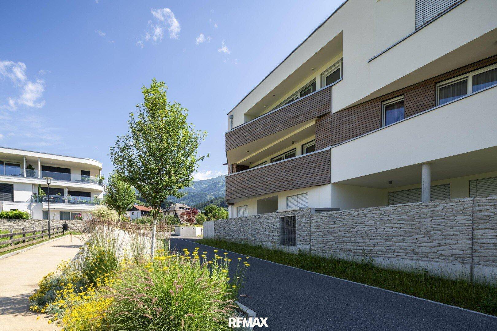 Moderne Wohngebäude mit Holzfassade und Balkonen, umgeben von gepflegten Grünflächen und einem Weg.