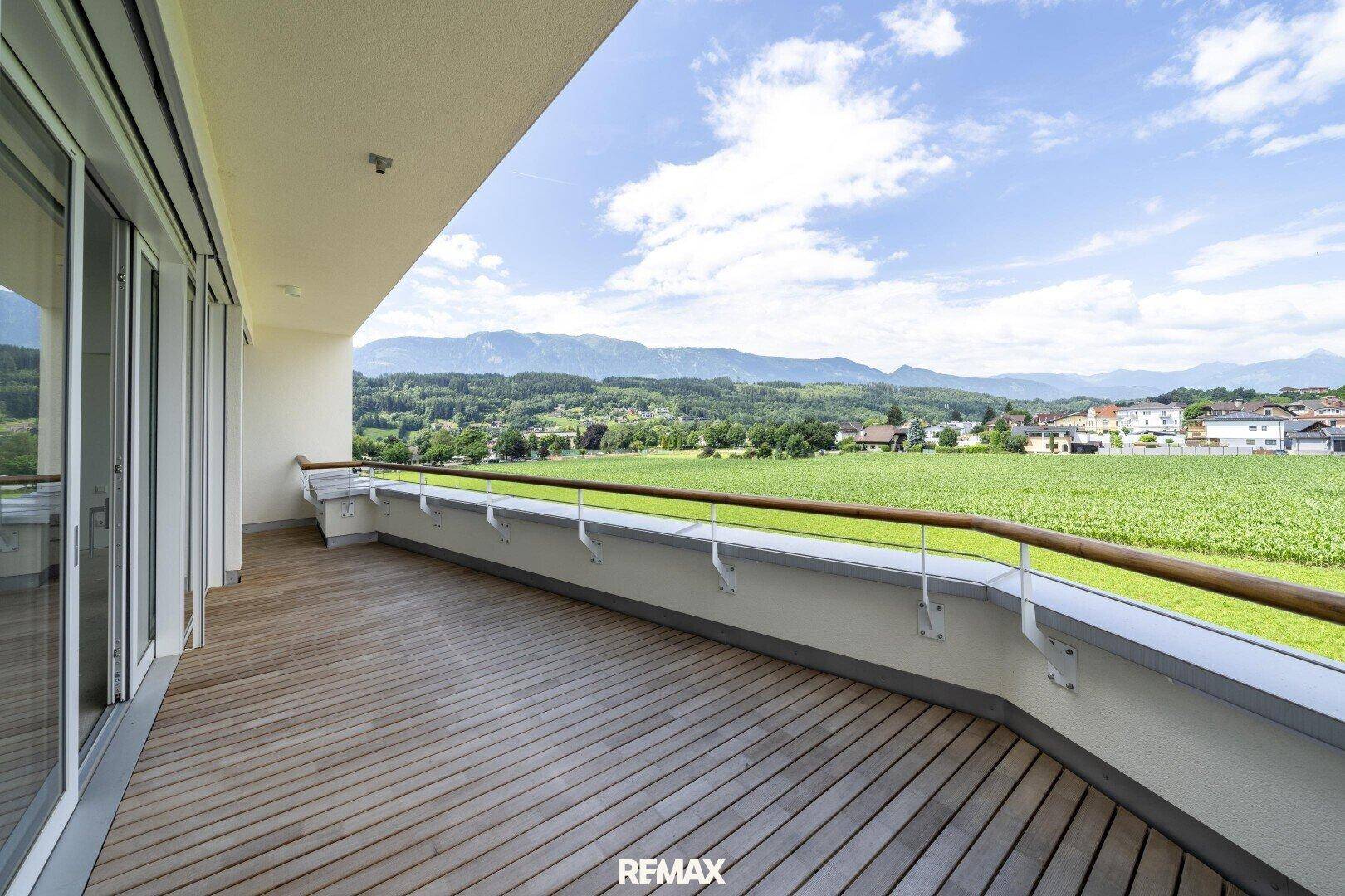 Geräumiger Balkon mit Holzfußboden und weitem Blick über grüne Felder und die umliegende Berglandschaft.