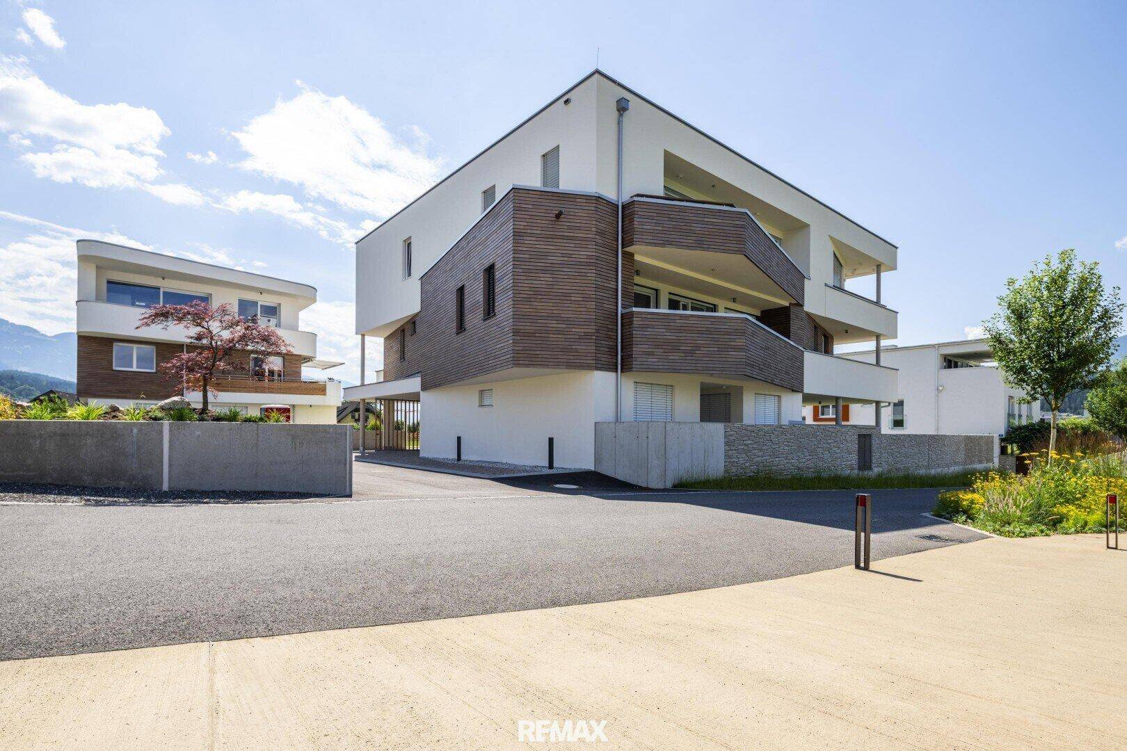 Außenansicht eines modernen Apartmentgebäudes mit weißer Fassade und Holzelementen sowie Zufahrt.