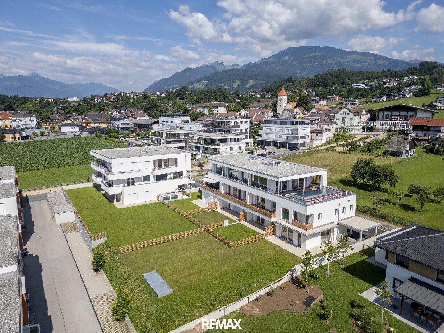 Panoramablick aus der Luft auf die moderne Wohnanlage, eingebettet in eine malerische Berg- und Seenlandschaft.