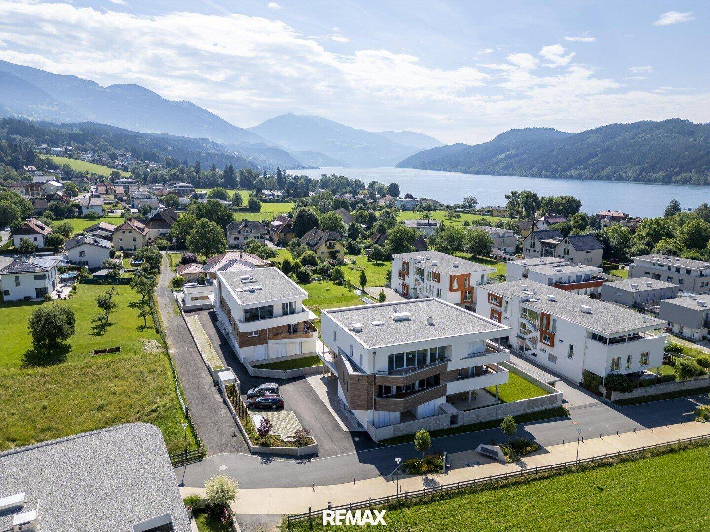 Luftaufnahme einer modernen Wohnsiedlung mit See- und Bergblick in einer malerischen Landschaft.