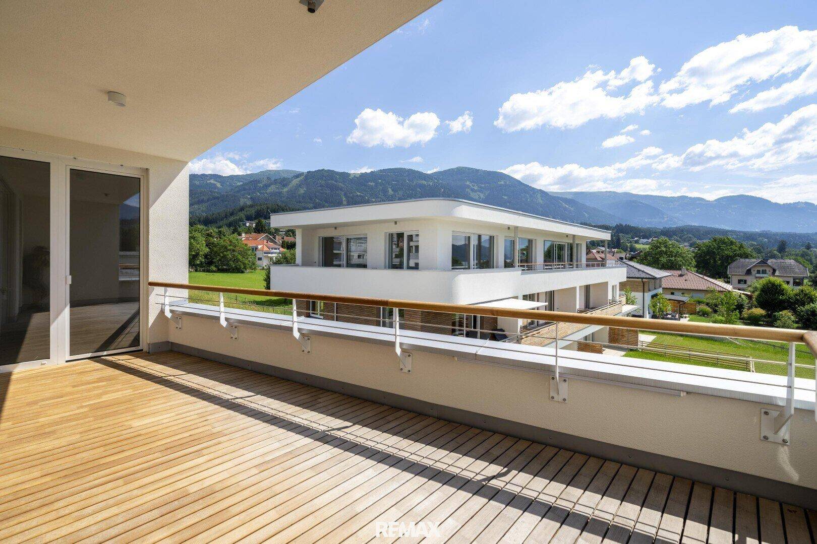 Heller Balkon mit Holzdielen und Panoramablick auf die Berge und moderne Architektur.