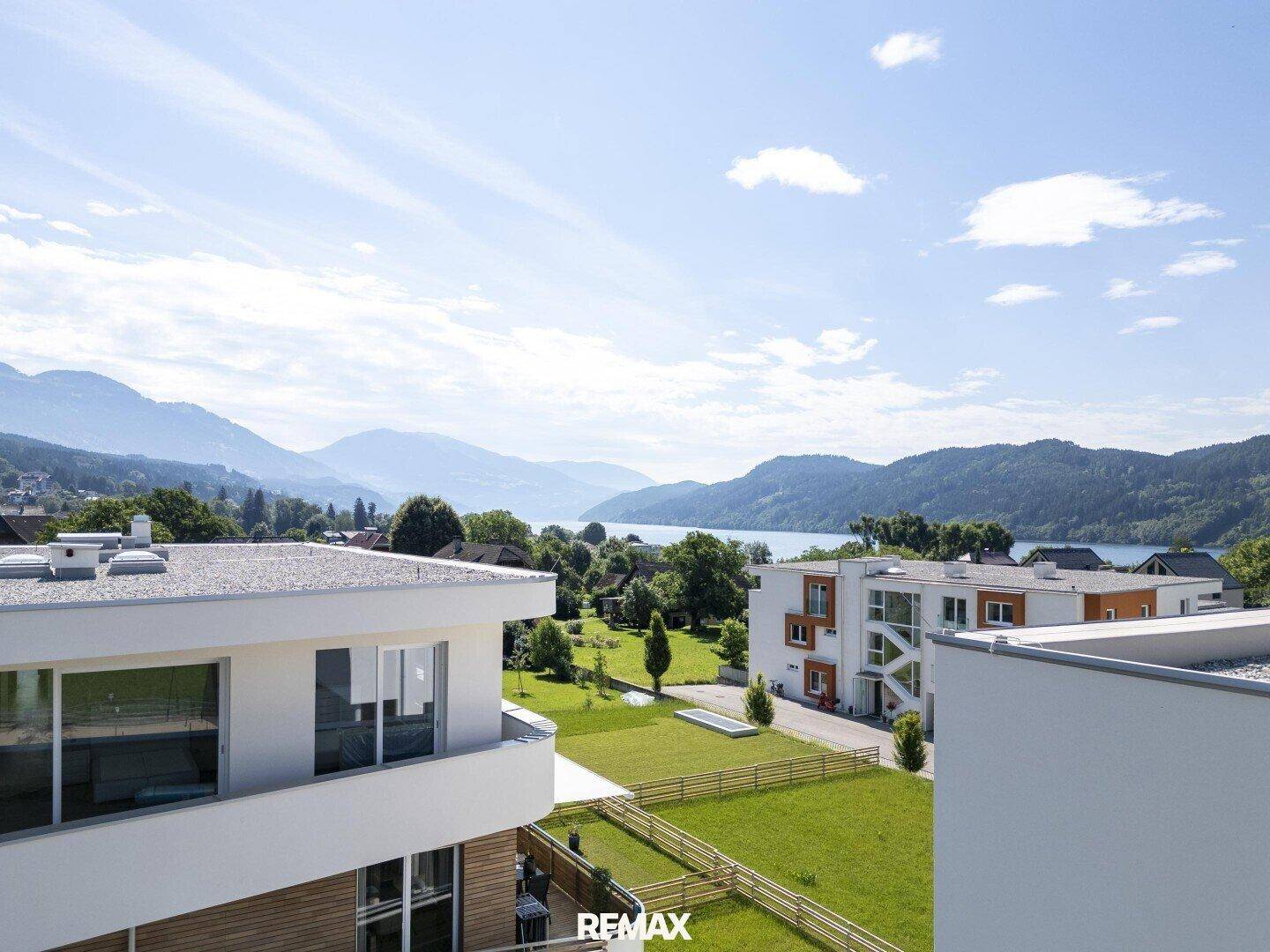 Weitläufiger Blick auf moderne Gebäude, einen See und die umliegende Berglandschaft.