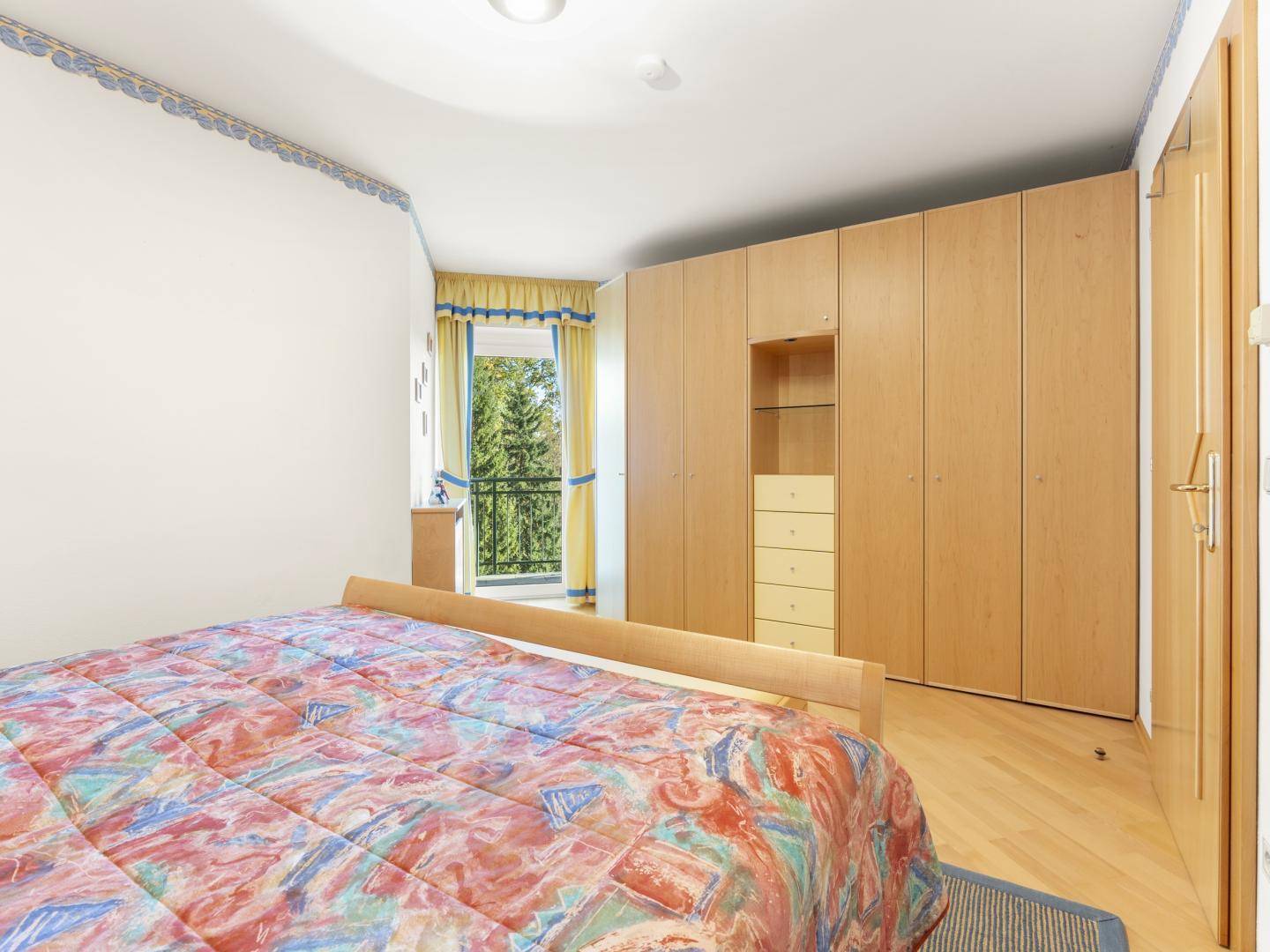 Schlafzimmer mit großem Einbauschrank, Parkettboden und Zugang zu einem kleinen Balkon.