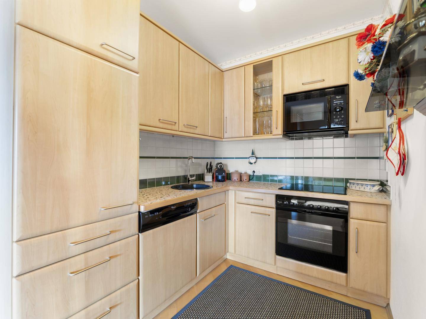 Funktionale Küche mit hellen Holzschränken, Fliesenrückwand und integrierten Geräten.