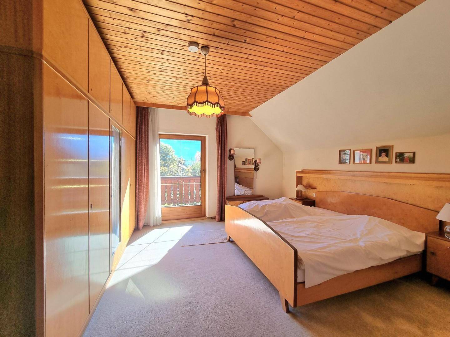 Helles Schlafzimmer im Dachgeschoss mit Einbauschränken, Balkonzugang und Holzboden.