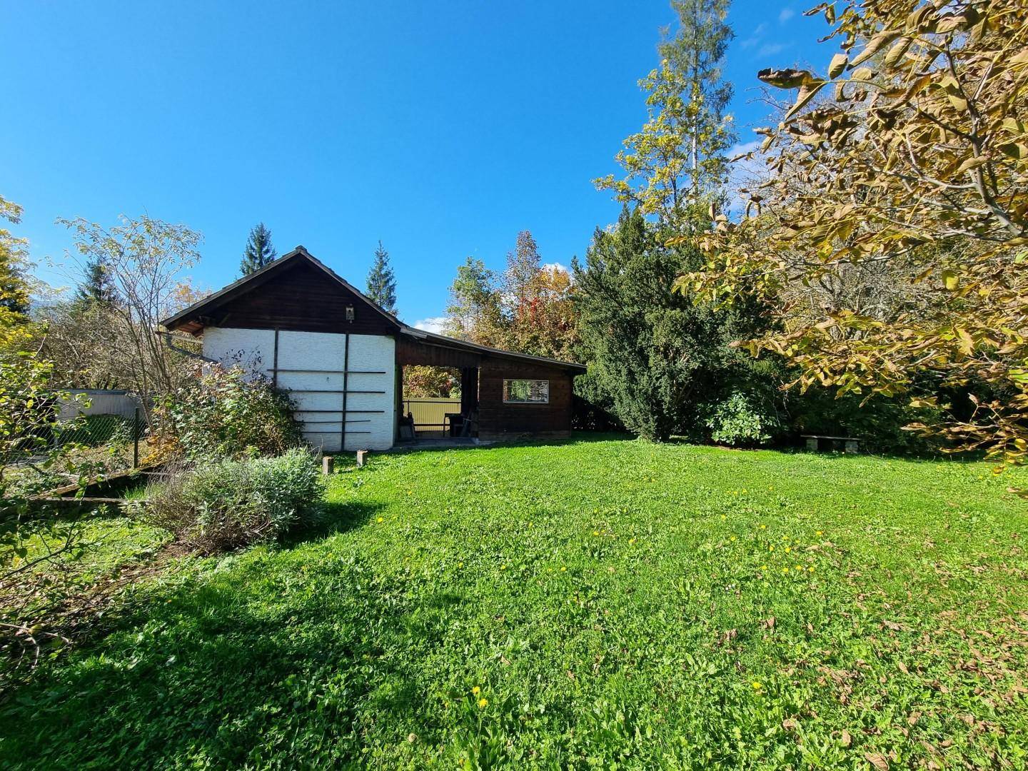 Großer, sonniger Gartenbereich mit einem kleinen Nebengebäude und viel Grünfläche.