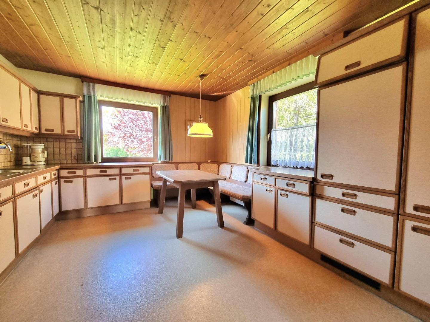 Gemütliche Wohnküche im Landhausstil mit Holztäfelung, Essecke und zwei Fenstern.