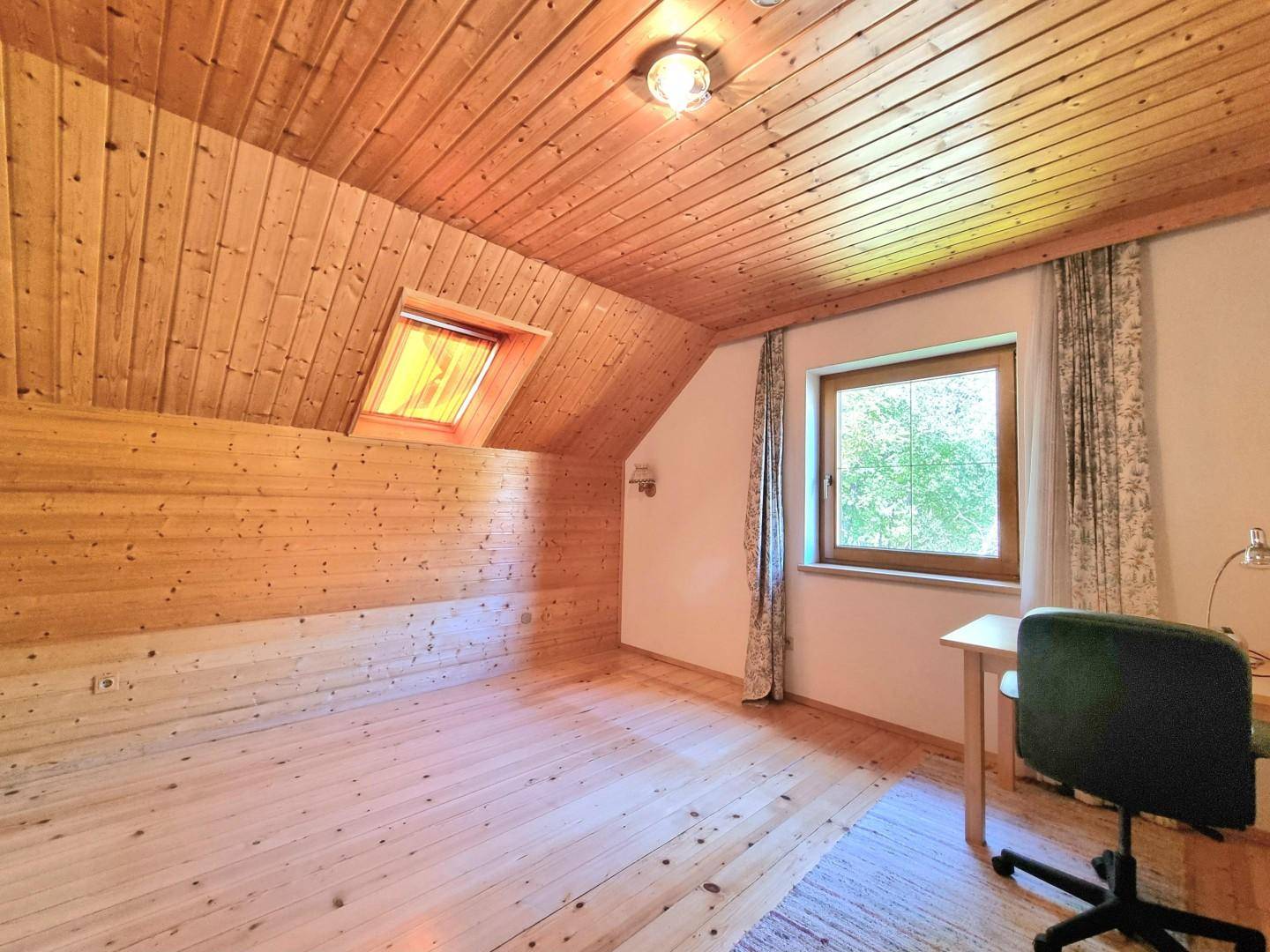 Dachzimmer mit Holzverkleidung, Dachfenster, hellem Holzboden und Schreibtisch.