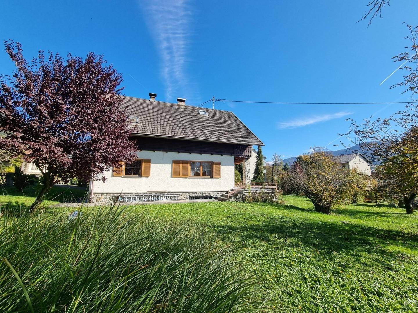 Seitenansicht des Hauses mit gepflegtem Rasen, Bäumen und sonnigem Wetter.