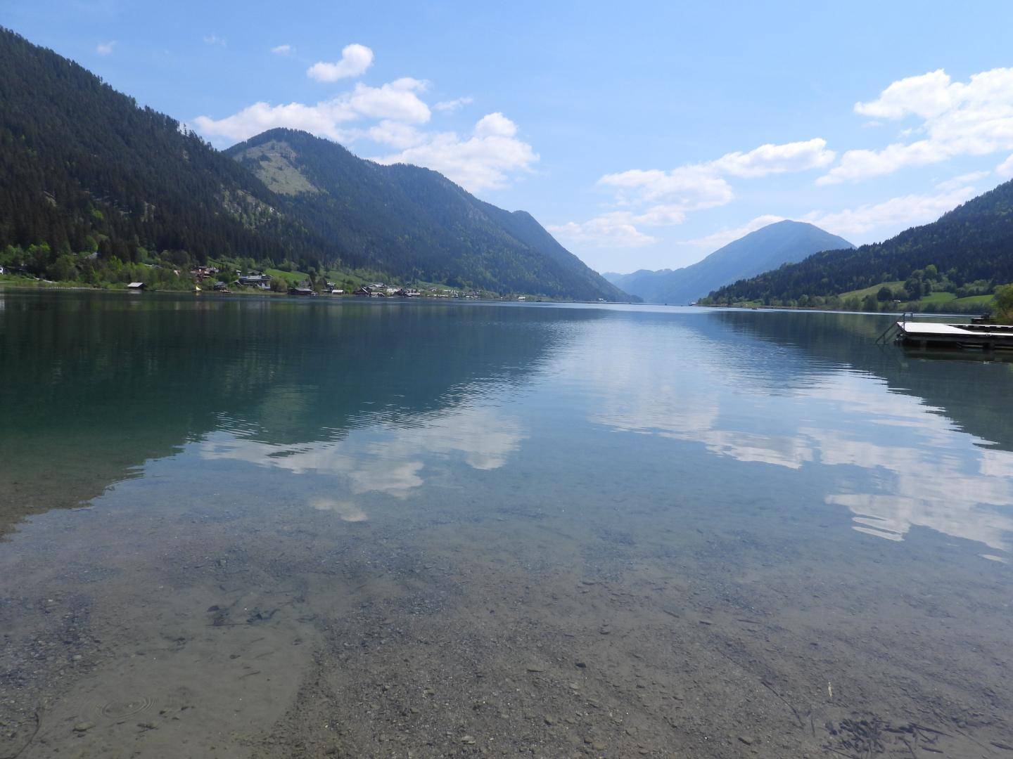 Weitläufiger Panoramablick über den tiefblauen See, umgeben von majestätischen Bergen unter klarem Himmel.