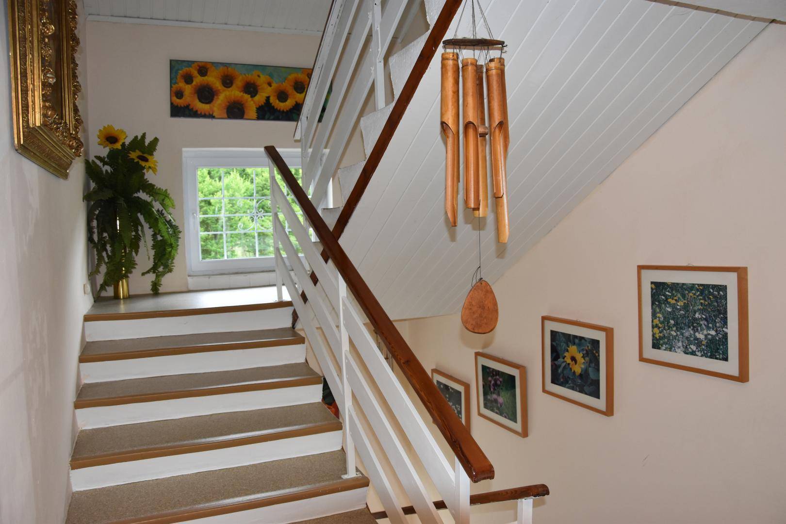 Helles Treppenhaus mit Holzstufen und weißem Geländer, dekoriert mit Sonnenblumenbildern, freundlich und einladend.