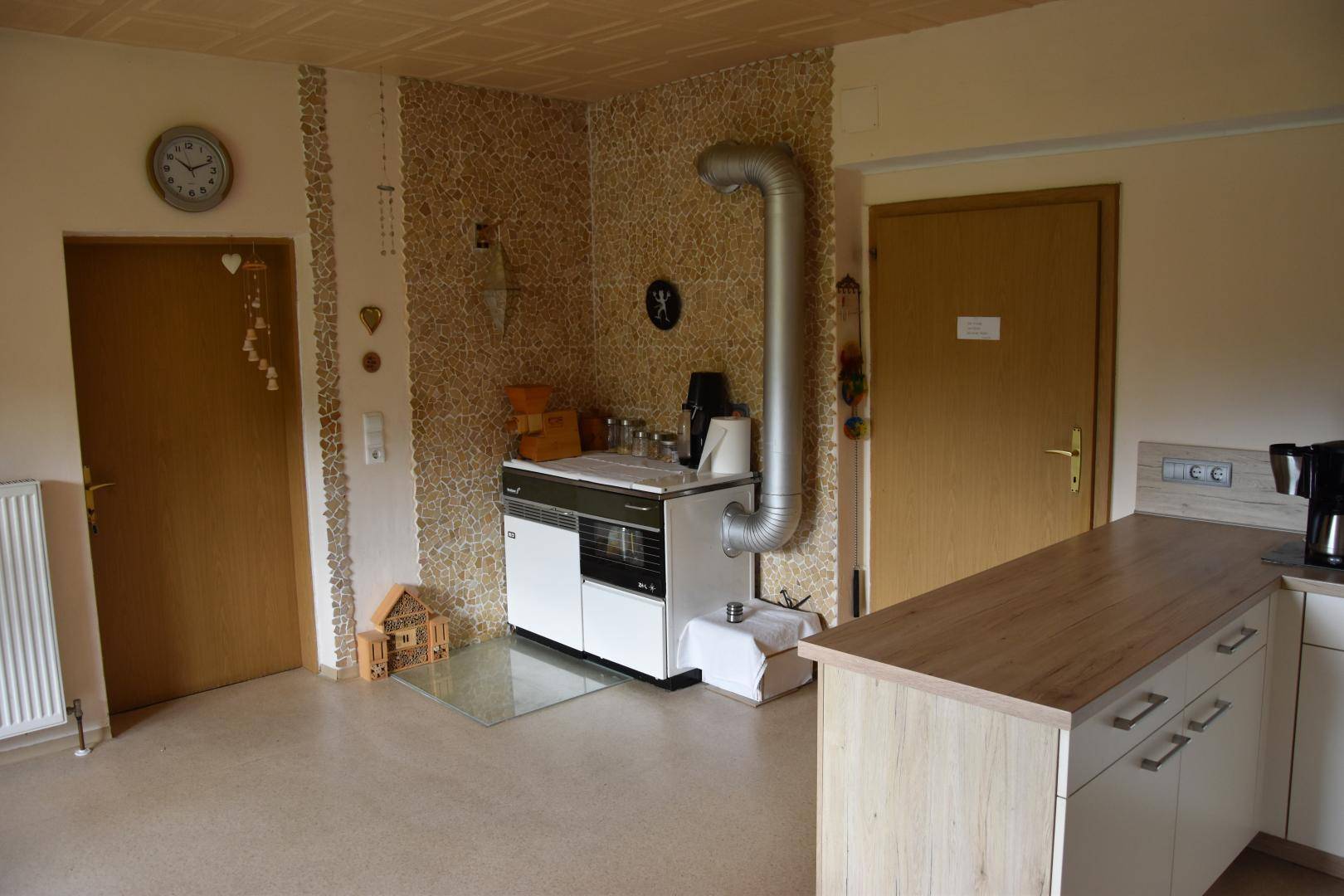 Küchenbereich mit traditionellem Holzofen, Arbeitsplatte und Schränken, daneben zwei Holztüren, rustikal eingerichtet.