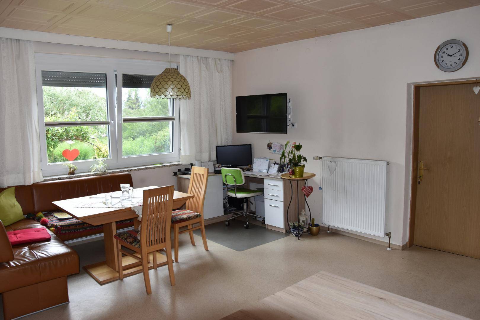 Wohn- und Essbereich mit Eckbank, Esstisch und einem Arbeitsplatz am Fenster mit Gartenblick, hell und funktional.