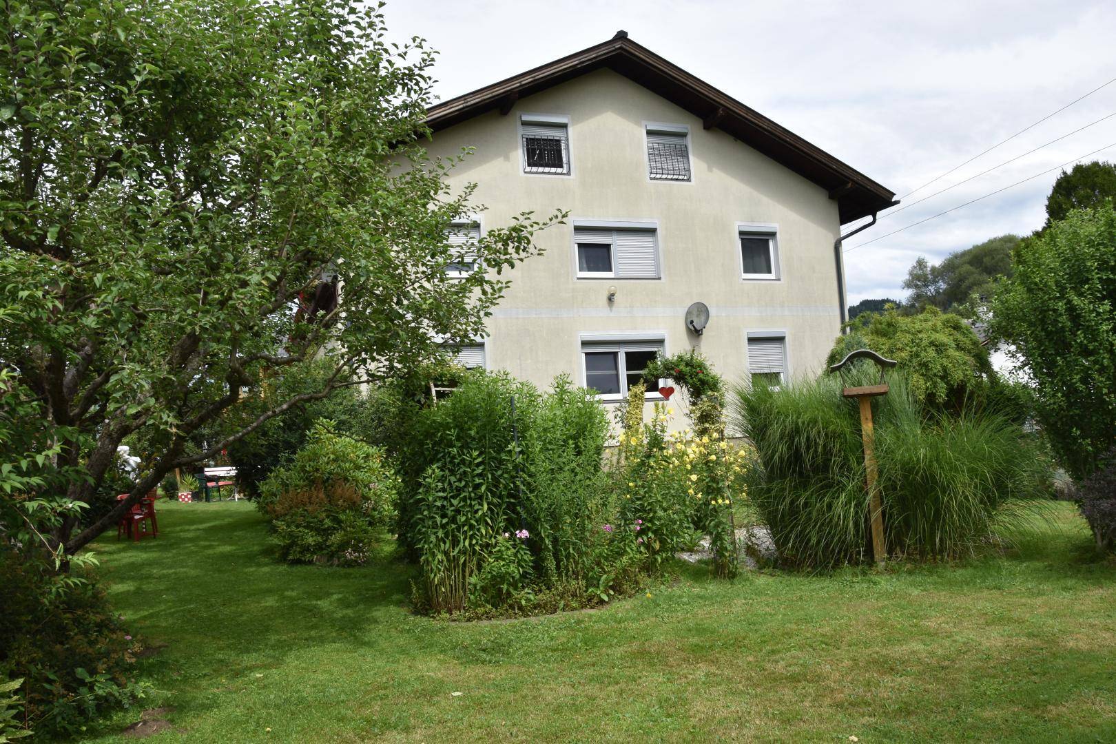 Großer, grüner Garten mit üppiger Vegetation, Bäumen und dem Haus im Hintergrund unter bewölktem Himmel.