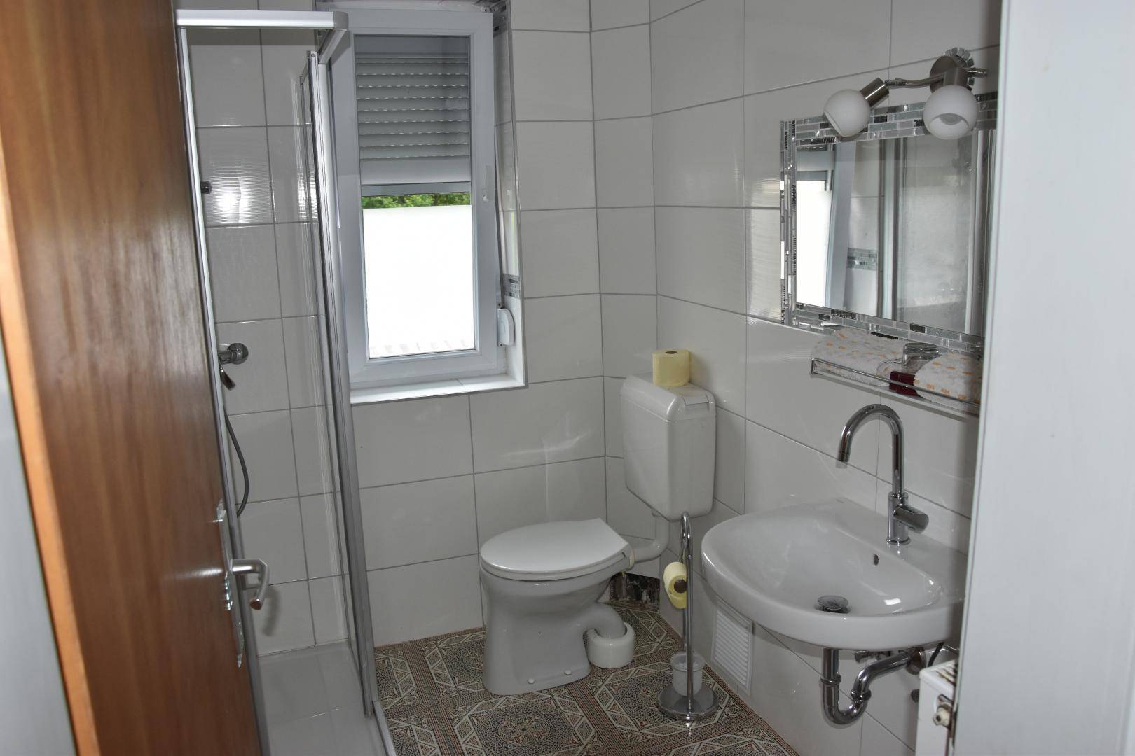 Modernisiertes Badezimmer mit Duschkabine, WC, Waschbecken und Fenster für natürliche Belüftung, hell und sauber.