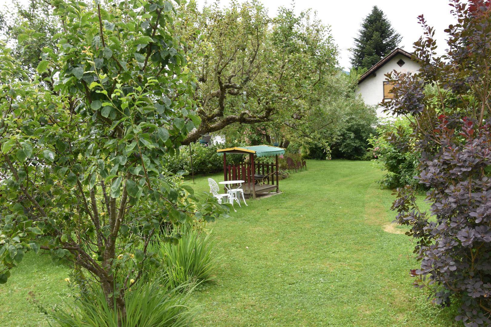 Großer, gepflegter Garten mit Rasenfläche, Bäumen und einer kleinen Sitzecke im Grünen, umgeben von Natur.