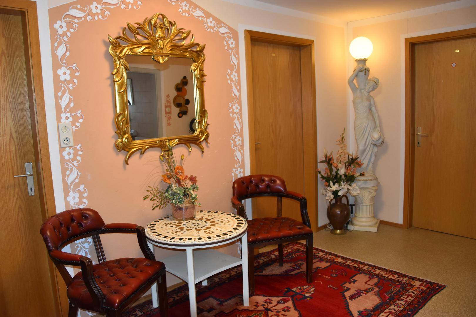 Eingangsbereich mit dekorativem Spiegel, zwei Sesseln und einer Stehlampe, traditionell und gemütlich eingerichtet.