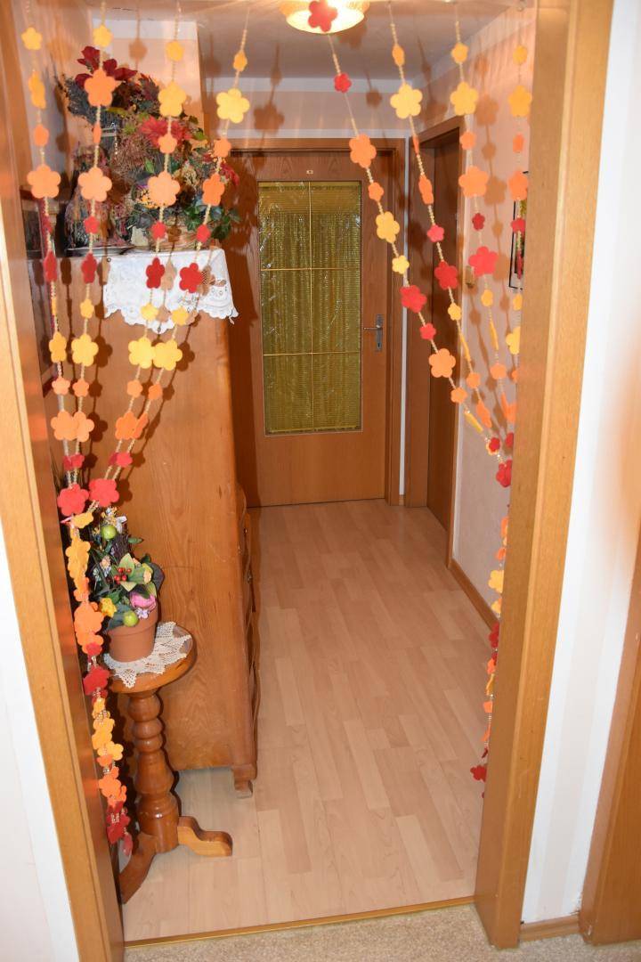 Heller Flur mit Laminatboden und einer Holztür, dekoriert mit bunten Girlanden, freundlich und einladend.
