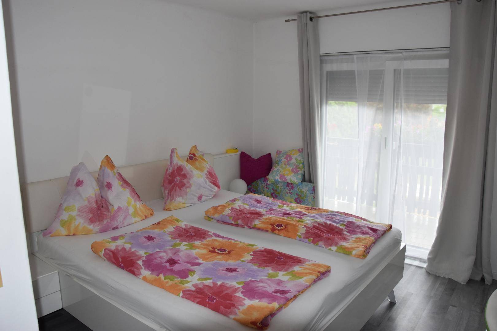 Modernes Schlafzimmer mit Doppelbett, floralen Bettbezügen und Zugang zum Balkon.