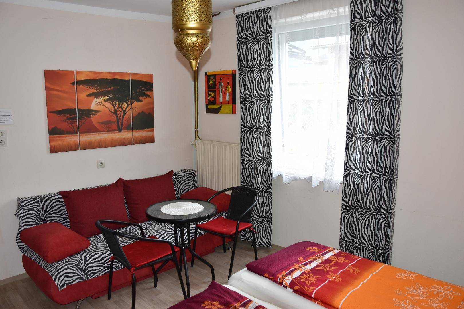 Schlafzimmer mit Schlafsofa, kleinem Tisch und auffälligen Zebra-Mustervorhängen.