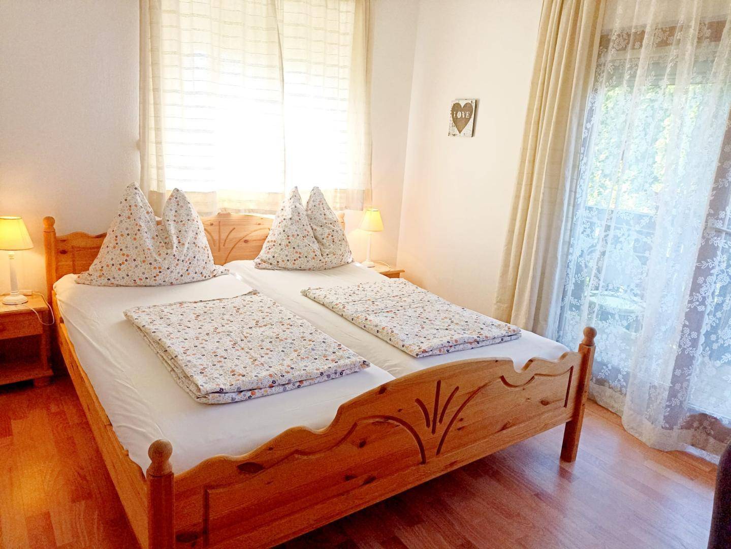 Helles Schlafzimmer mit zwei Einzelbetten, Holzrahmen und Zugang zum Balkon.