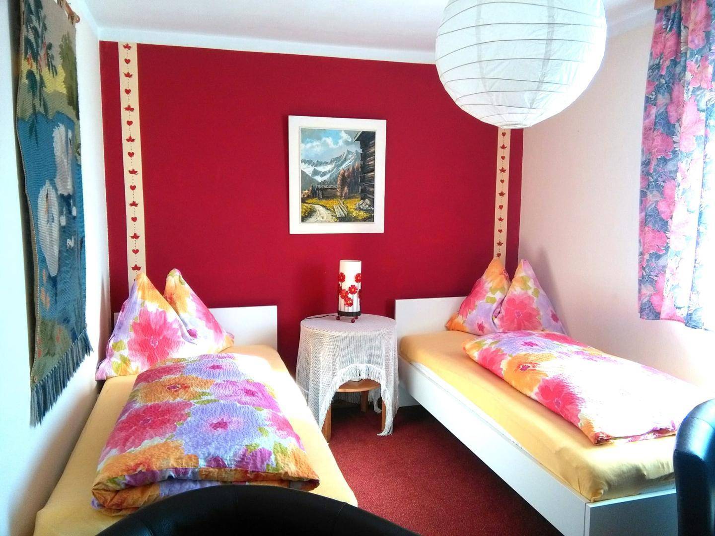 Schlafzimmer mit zwei Einzelbetten, roter Akzentwand und traditioneller Dekoration.