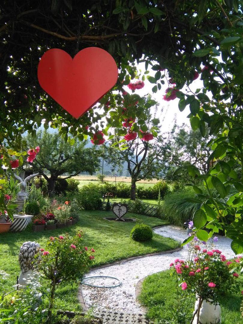 Romantischer Gartenweg mit Kies, Blumenbeeten und einem großen roten Herz als Dekoration.