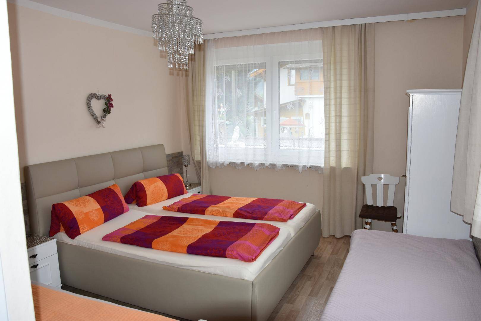 Helles Schlafzimmer mit Doppelbett, Nachttischen und einem Kronleuchter.